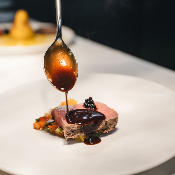 Sensoria Dolomites: Wellnesshotel in den Dolomiten Sauce wird auf ein Stück rosa gebratenes Fleisch mit Gemüse geträufelt