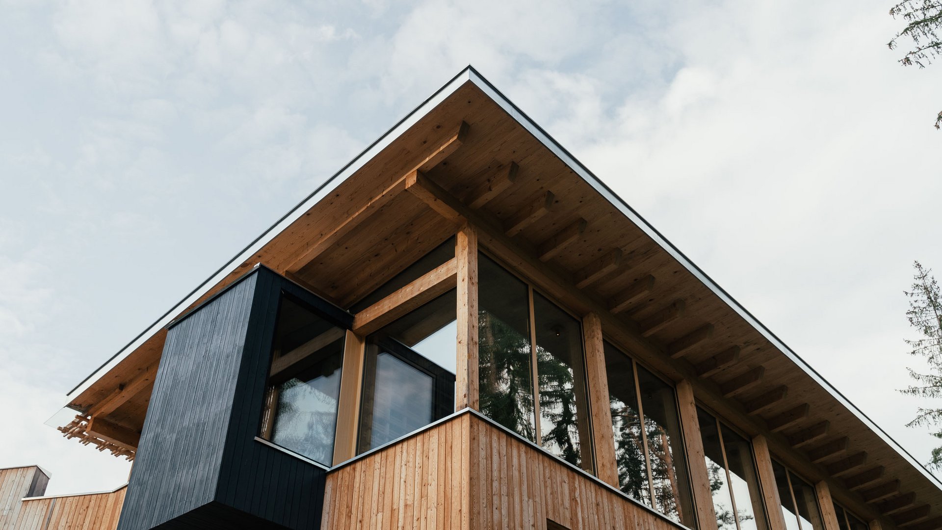Sensoria Dolomites: Wellnesshotel in den Dolomiten Moderner Holzhausgiebel mit großen Fenstern und schwarzem Vorsprung bei bewölktem Himmel