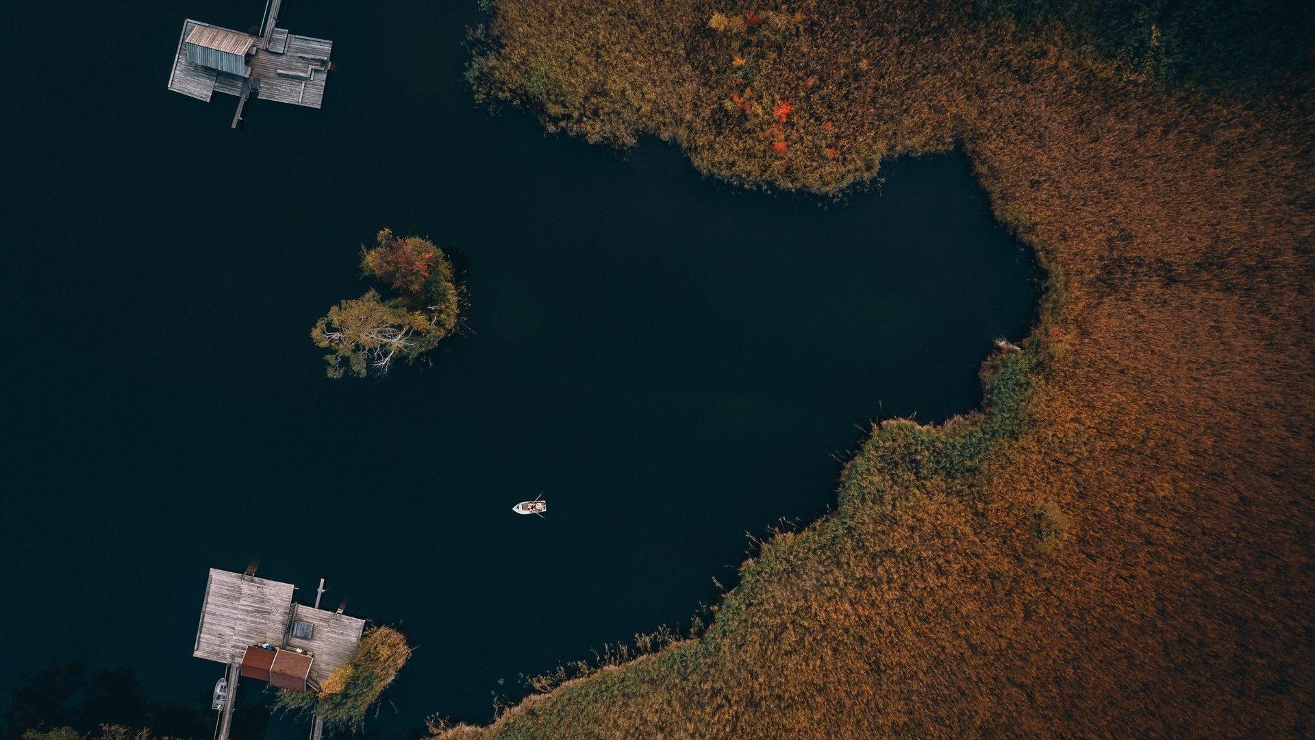 Meteo all’Alpe di Siusi? Soleggiato! Vista aerea di un lago scuro con moli, isola e barca