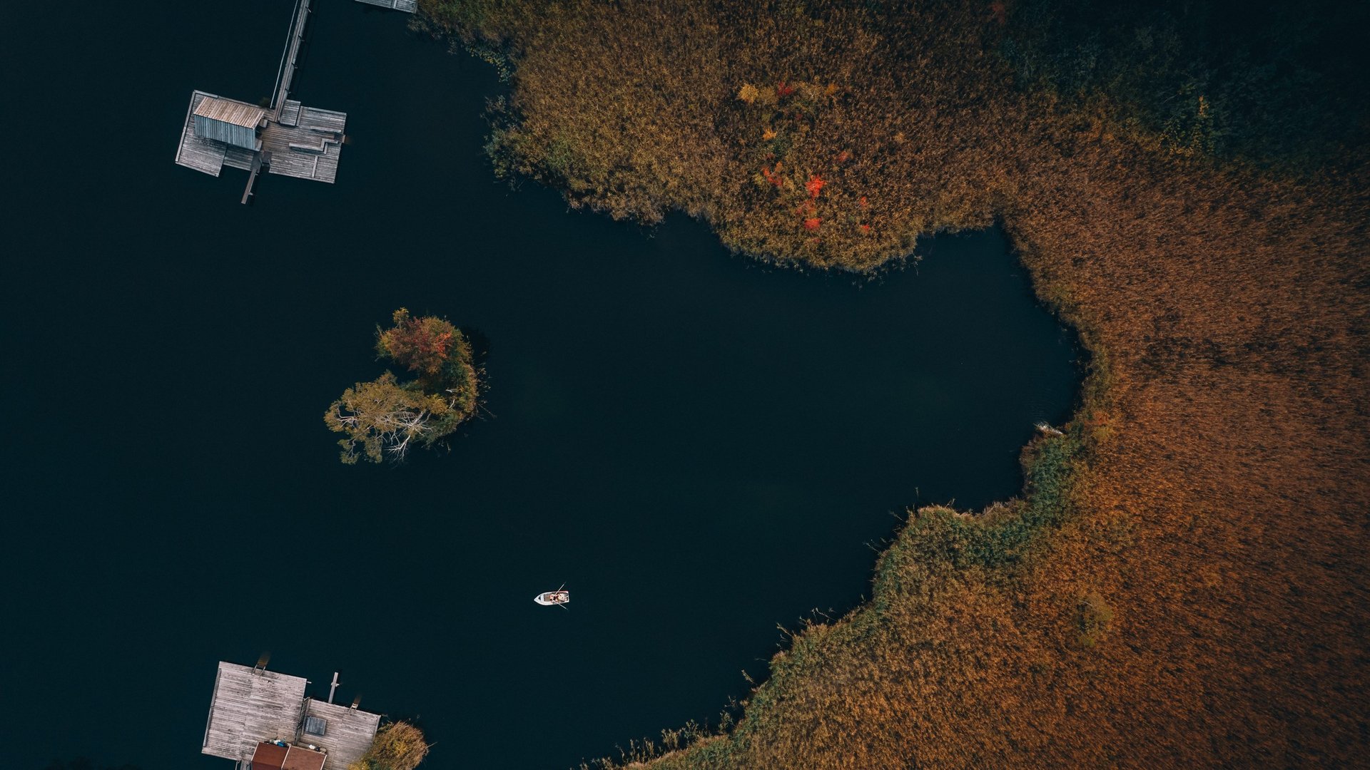 Active holidays in South Tyrol – ready for pure nature? Aerial view of a dark lake with docks, island, and boat