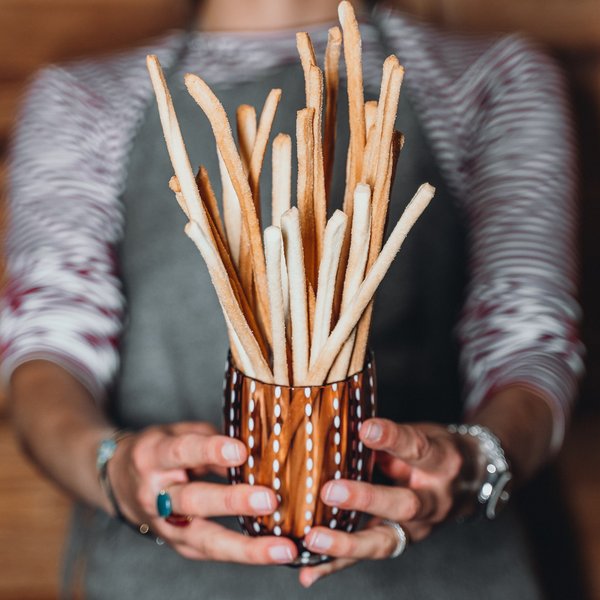Sustainability at Sensoria Dolomites Person holding a glass filled with long crispy breadsticks grissini