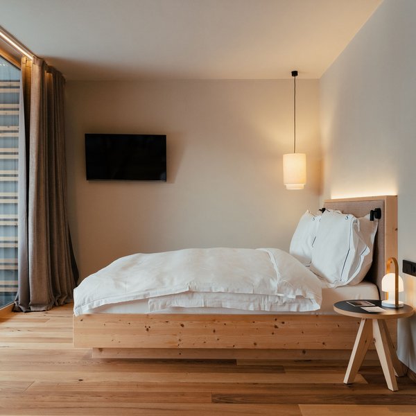Sensoria Dolomites: il vostro hotel sull’Alpe di Siusi Camera da letto moderna con letto matrimoniale, dettagli in legno e grande finestra sulla terrazza