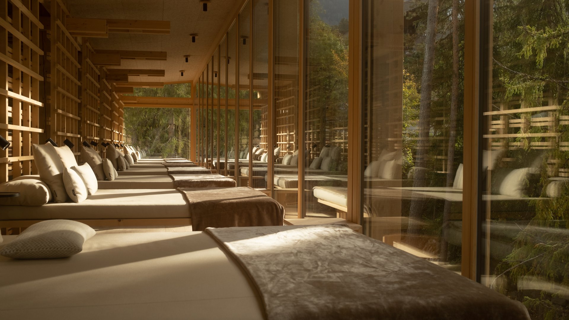 Wellness Aphrodite: Sensoria Dolomites among the winners Relax beds with pillows and blankets in a wooden room with glass windows and forest view