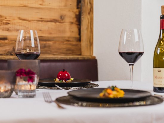 Golf und Wellness – Ihr Golfhotel nahe der Seiser Alm Tisch mit Weinflasche, zwei Weingläsern und Gourmetdessert in einem Restaurant