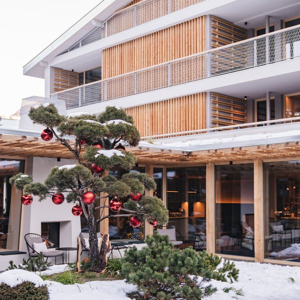 Sensoria Dolomites: il vostro hotel sull’Alpe di Siusi Edificio moderno in legno con giardino innevato e albero decorato con palline rosse