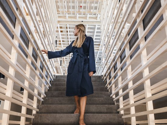 Naturhotel in Südtirol. Luxus für die Seele. Frau in blauem Bademantel geht barfuß eine Treppe in modernem Holzrahmenhaus hinauf