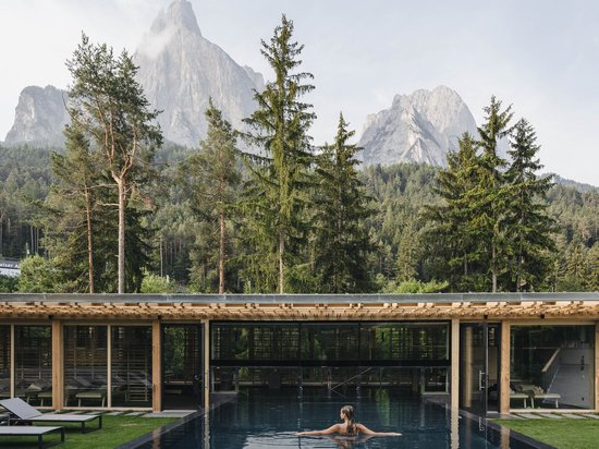 Vacanza e golf: accoppiata vincente Donna nella piscina davanti a edificio in legno con montagne e alberi sullo sfondo