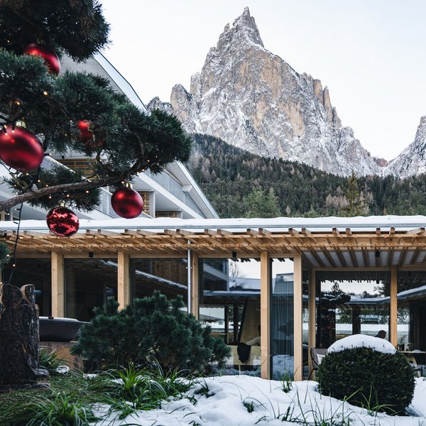 Sensoria Dolomites: il vostro hotel sull’Alpe di Siusi Hotel innevato con decorazioni natalizie davanti a montagne innevate