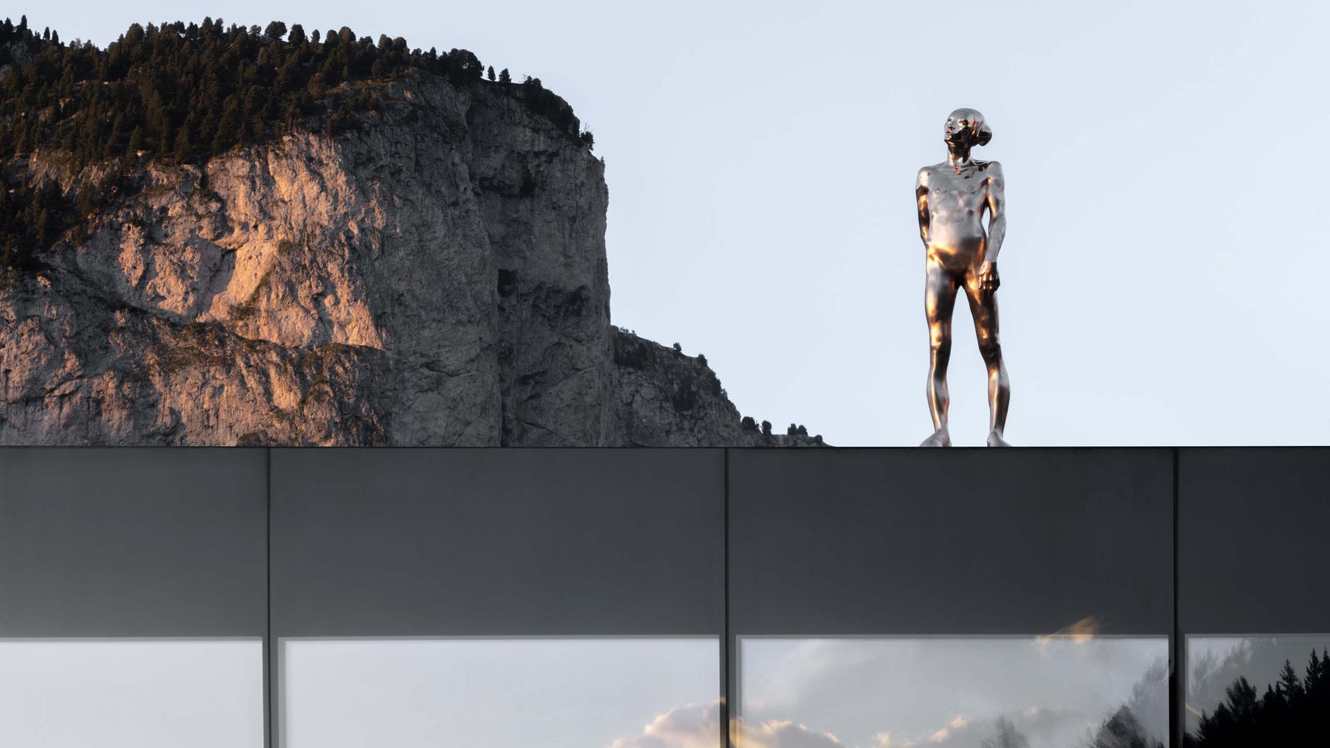 Reflective statue on building with mountain backdrop at sunset