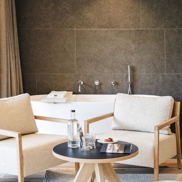 Sensoria Dolomites: Wellnesshotel in den Dolomiten Zwei beige Sessel und ein Tisch vor einer Badewanne mit dunkler Wand