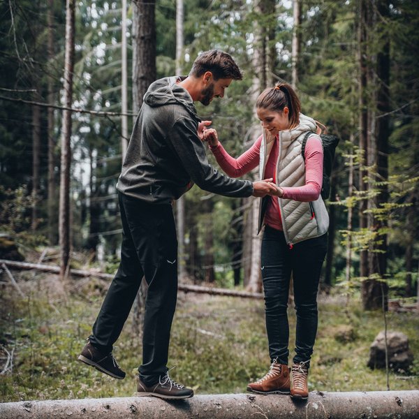 Active holidays in South Tyrol – ready for pure nature? Man helping woman balance on a log in the forest