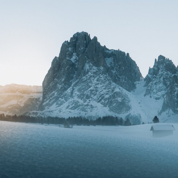 Active holidays in South Tyrol – ready for pure nature? Snow-covered mountain at sunrise with cabin and trees in the foreground
