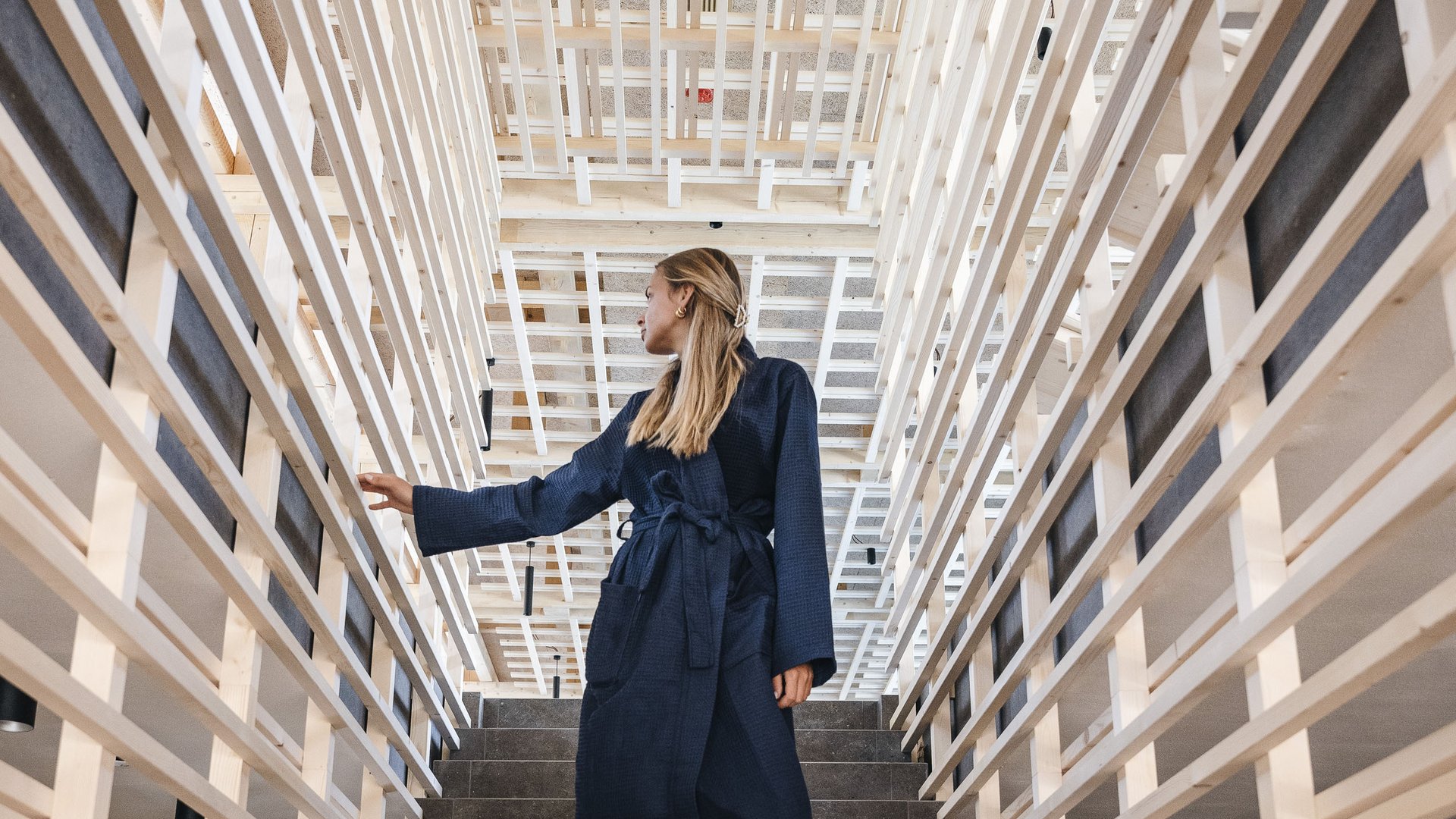 Wellness Aphrodite: Sensoria Dolomites among the winners Woman in bathrobe walks barefoot down stairs with wooden railings