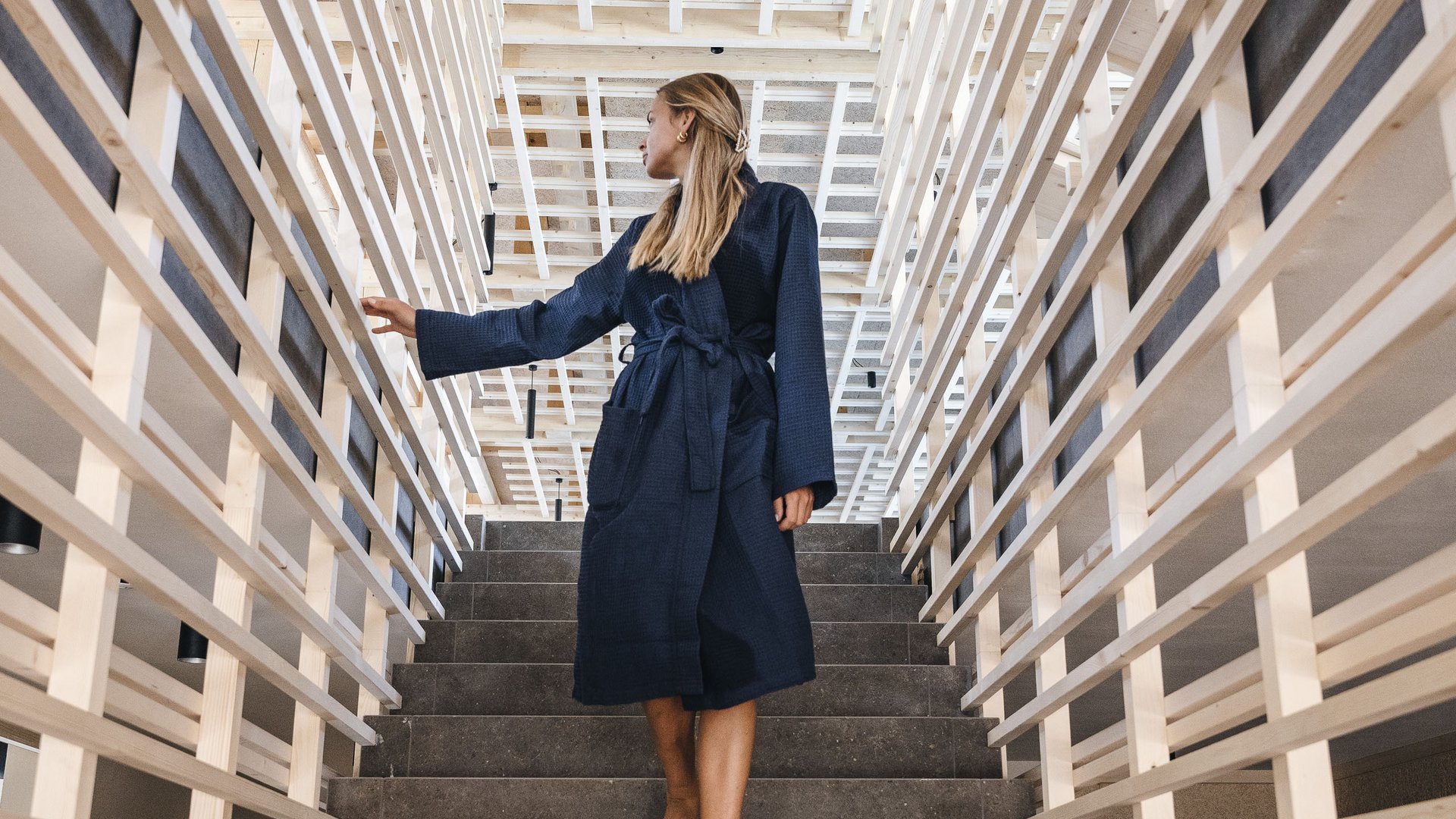 Wellness Aphrodite: Sensoria Dolomites tra i vincitori Donna in accappatoio scende scale a piedi nudi con ringhiere di legno