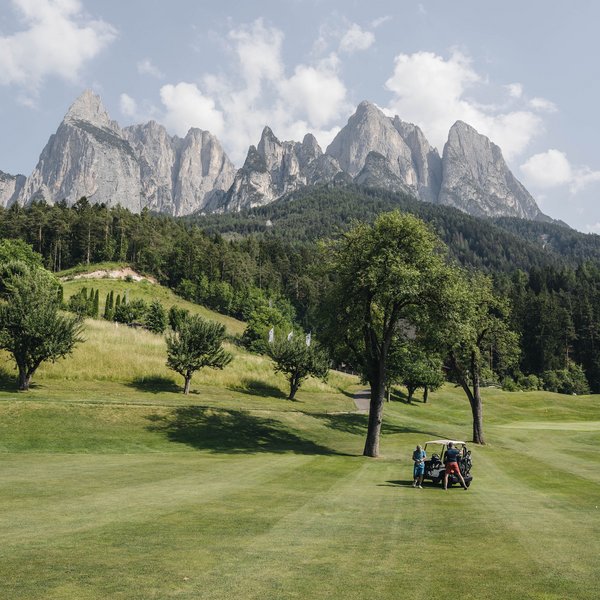 Sensoria Dolomites: Wellnesshotel in den Dolomiten Golfspieler auf grünen Fairway mit Dolomiten-Bergpanorama im Hintergrund