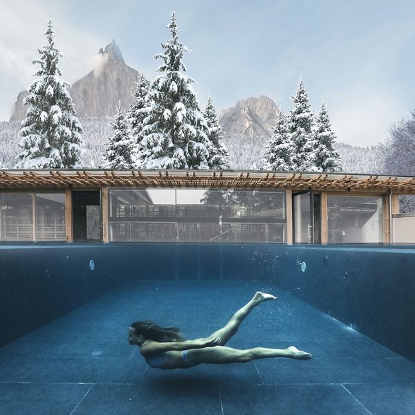 Sensoria Dolomites: il vostro hotel sull’Alpe di Siusi Donna nuota sott'acqua in una piscina con alberi innevati e montagne sullo sfondo