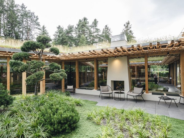Wellness Aphrodite: Sensoria Dolomites among the winners Modern garden with patio, fireplace, wooden pergola surrounded by trees