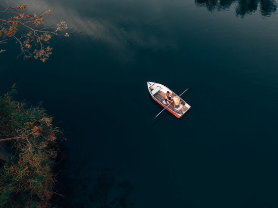 Hotel a Siusi allo Sciliar? Sensoria Dolomites! Due persone sedute su una barca su acqua calma vicino alla riva con vegetazione