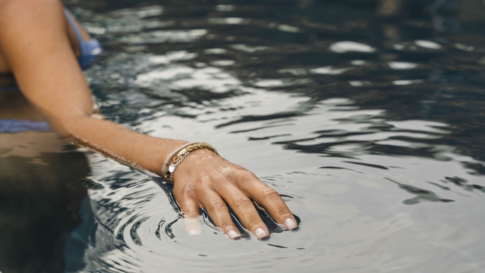 Erholung in und mit der Natur – Ihr Spa-Hotel in Südtirol Frau mit Armband im Wasser berührt die Wasseroberfläche im Pool
