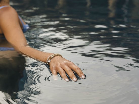 Hotel all’Alpe di Siusi: un tempio di energia per l’anima Donna con braccialetto tocca la superficie dell'acqua in piscina
