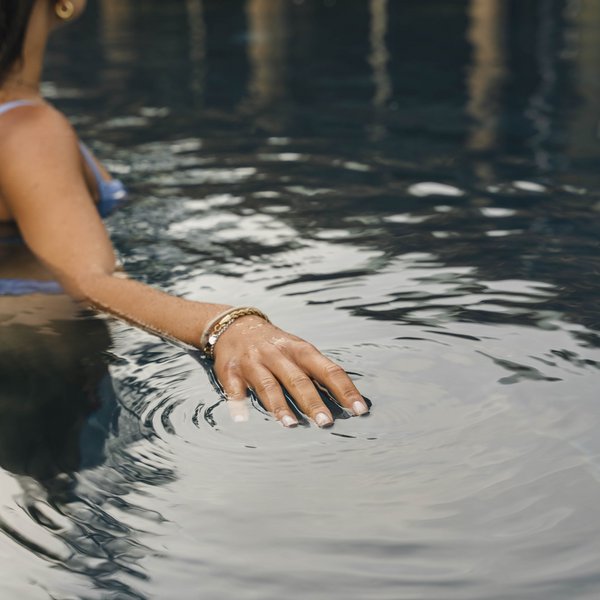 Sensoria Dolomites: Wellnesshotel in den Dolomiten Frau mit Armband im Wasser berührt die Wasseroberfläche im Pool