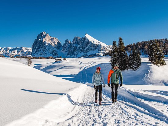 Hotel in Seis am Schlern gesucht? Sensoria Dolomites gefunden! Zwei Personen wandern auf einem verschneiten Weg in den Bergen bei Sonnenschein