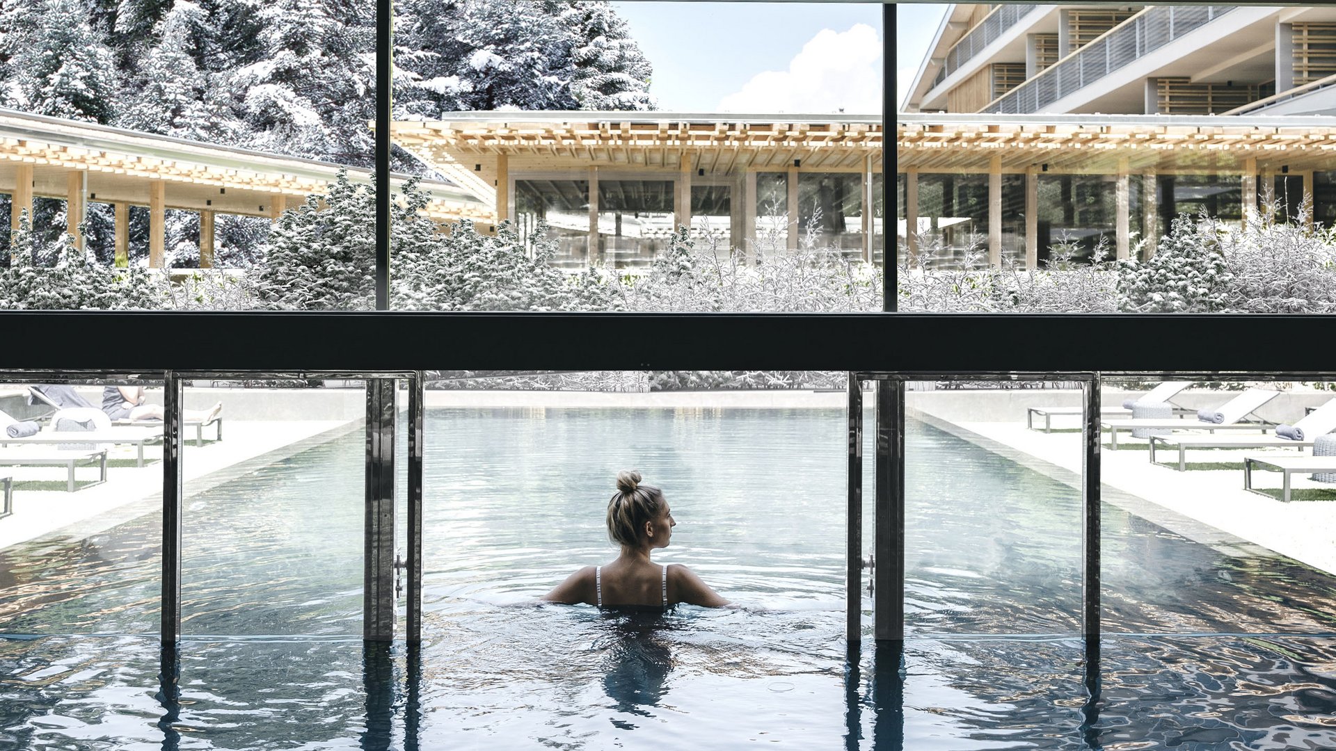 Day Spa in Südtirol – Wellness für die Seele Frau entspannt im Innenpool mit Blick auf verschneite Landschaft und Gebäude