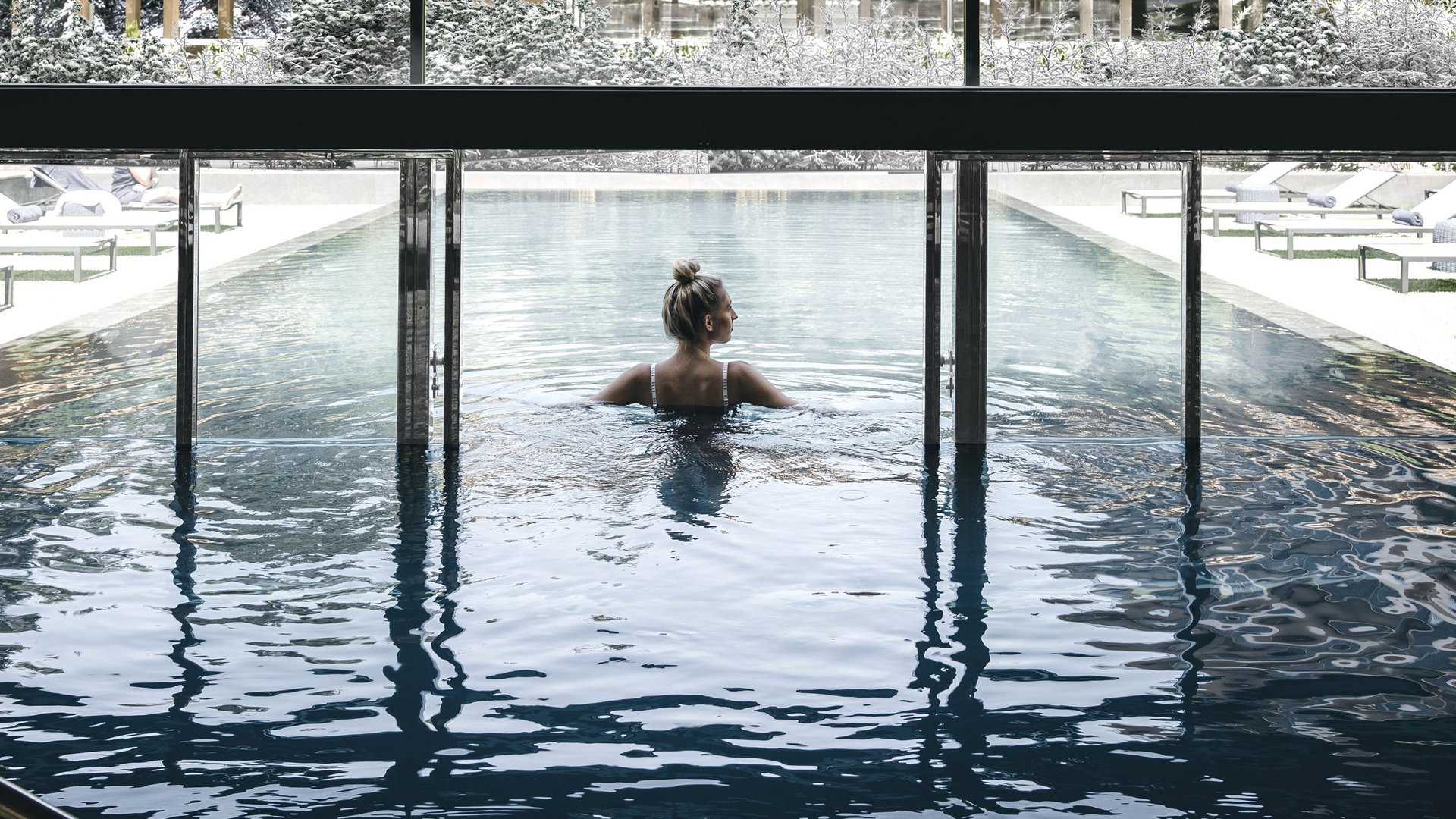Wellness Aphrodite: Sensoria Dolomites tra i vincitori Donna rilassata in piscina interna con vista su paesaggio innevato e edifici