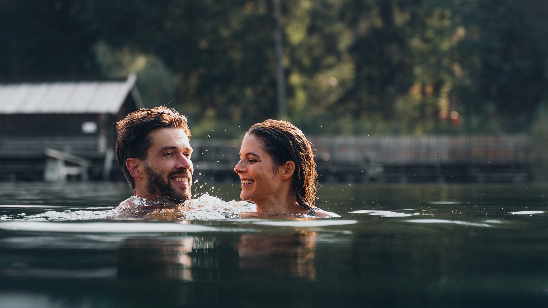 A summer holiday in the mountains Happy couple swimming in a lake with forest and cabin in the background