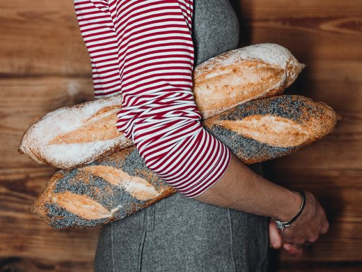 Sustainability at Sensoria Dolomites Woman holding four baguettes in arms in front of wooden wall