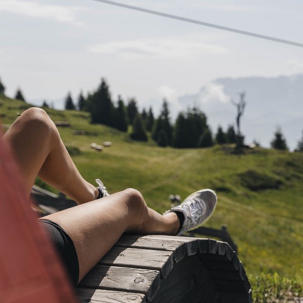 Active holidays in South Tyrol – ready for pure nature? Person relaxing on wooden structure overlooking green meadows and trees
