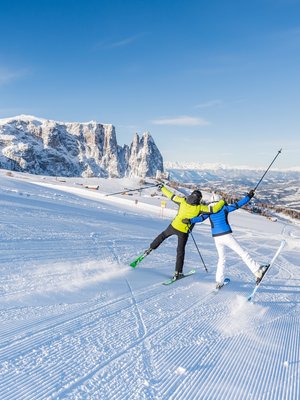 Luxus für die Seele im Kurzurlaub in Südtirol Zwei Skifahrer in bunten Jacken fahren auf verschneiter Piste mit Bergkulisse