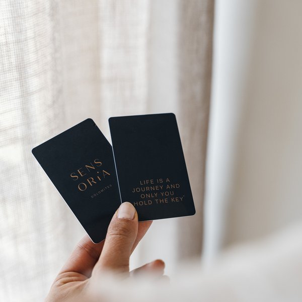 Romantischer Kurzurlaub für Verliebte – Sensoria Dolomites Hand hält zwei schwarze Karten mit goldener Schrift vor einem Vorhang