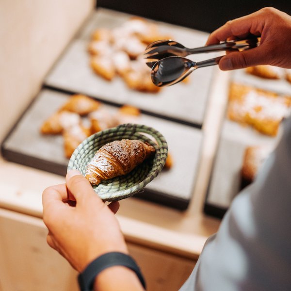 Sensoria Dolomites: Wellnesshotel in den Dolomiten Person nimmt Croissant mit Zangen aus Körbchen