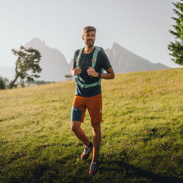 Active holidays in South Tyrol – ready for pure nature? Man with backpack hiking in a green mountain meadow under the sun