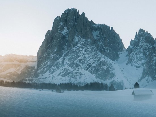 Kraftorte in Südtirol Schneebedeckte Bergspitze bei Sonnenaufgang mit Holzhütte im Vordergrund