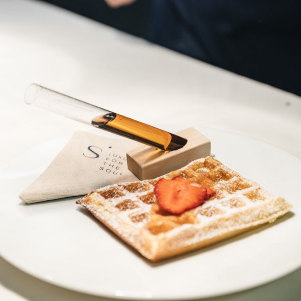 Sensoria Dolomites: Wellnesshotel in den Dolomiten Waffel mit Puderzucker und Erdbeere, neben Glasröhrchen mit Sirup