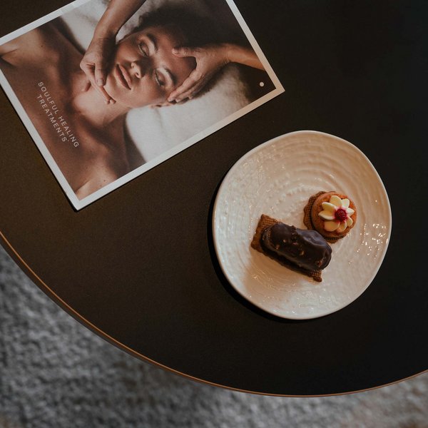 Sensoria Dolomites: Wellnesshotel in den Dolomiten Zwei Kekse auf weißem Teller und Wellnessbroschüre auf schwarzem Tisch