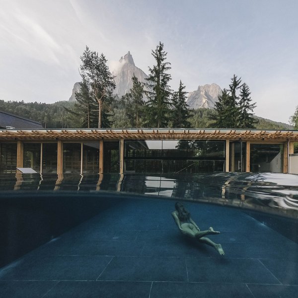 Sensoria Dolomites: Flitterwochen in Südtirol Frau schwimmt unter Wasser in Pool vor Bergkulisse und modernem Gebäude