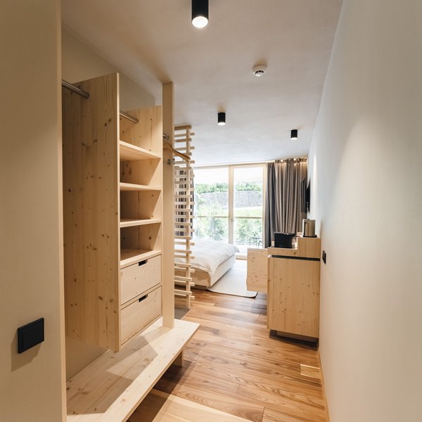 Romantischer Kurzurlaub für Verliebte – Sensoria Dolomites Heller Hotelzimmerflur mit Holzmöbeln und Blick auf Doppelbett und Balkon