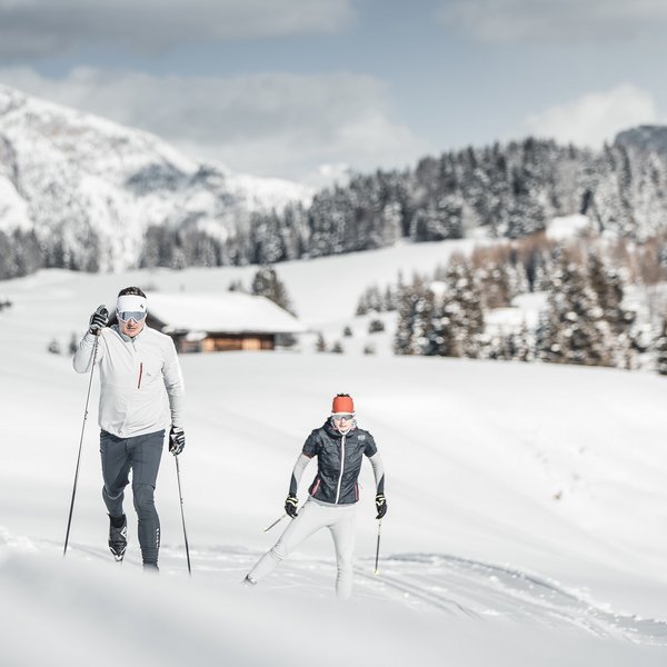 Settimana bianca sulle Dolomiti, al Sensoria Dolomites Due persone fanno sci di fondo in paesaggio montano innevato con baita