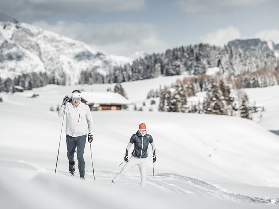 Active holidays in South Tyrol – ready for pure nature? Two people cross-country skiing in snowy mountain landscape with cabin