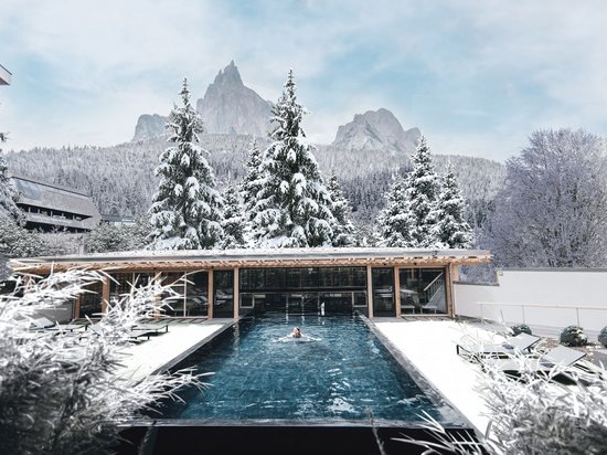 Luxus für die Seele im Kurzurlaub in Südtirol Frau schwimmt in Outdoor-Pool mit verschneiten Bäumen und Bergen im Winter