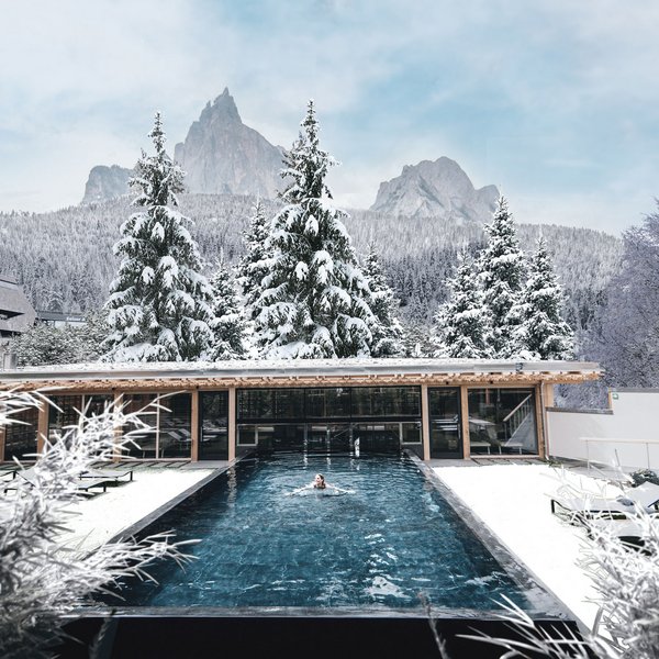 Hotel in mezzo alla natura: area spa del Sensoria Dolomites Donna che nuota in piscina all'aperto con alberi innevati e montagne in inverno