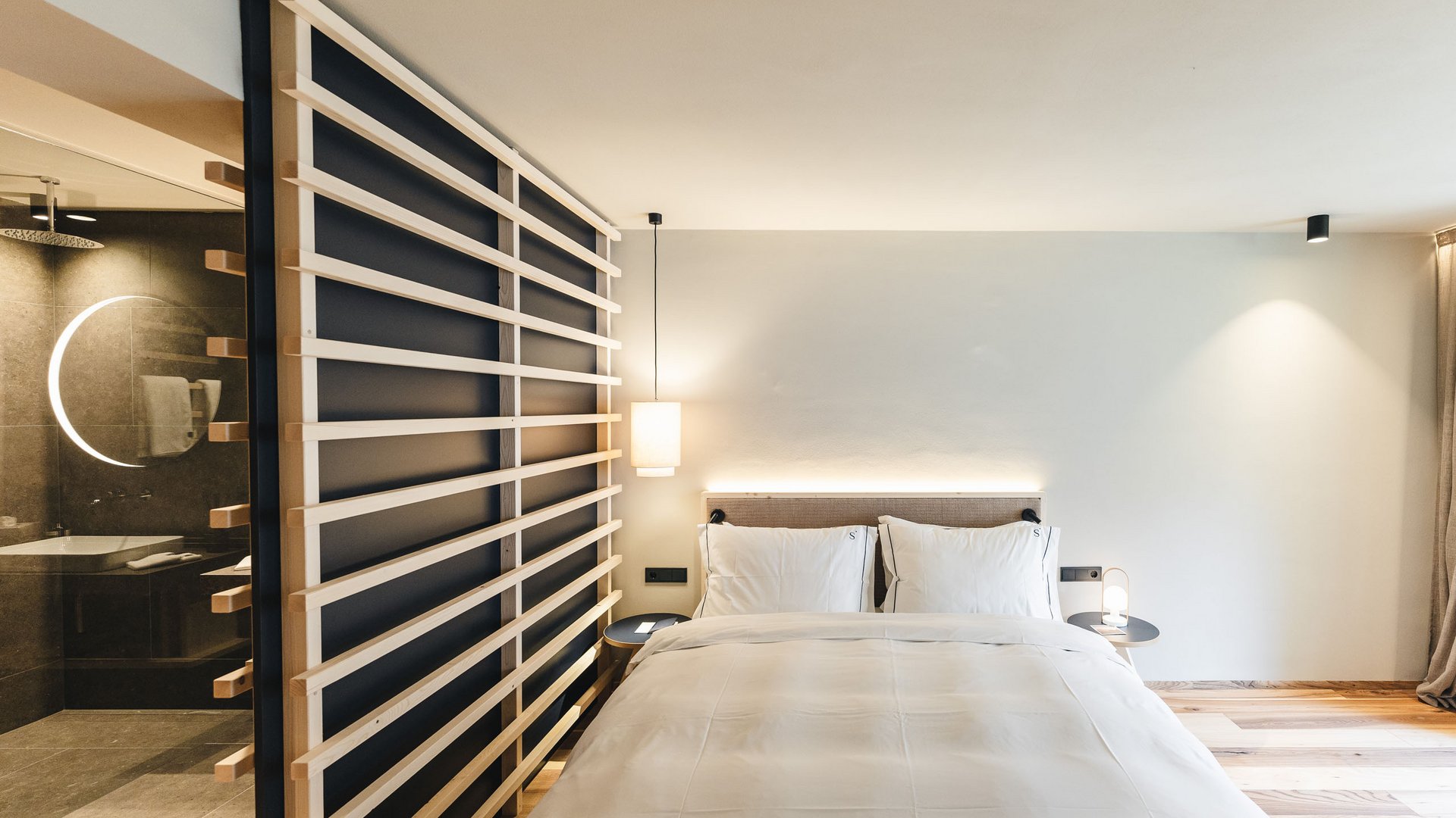 Dormire a Siusi allo Sciliar: la vostra camera preferita Camera da letto moderna con letto bianco e parete in legno separatrice dal bagno