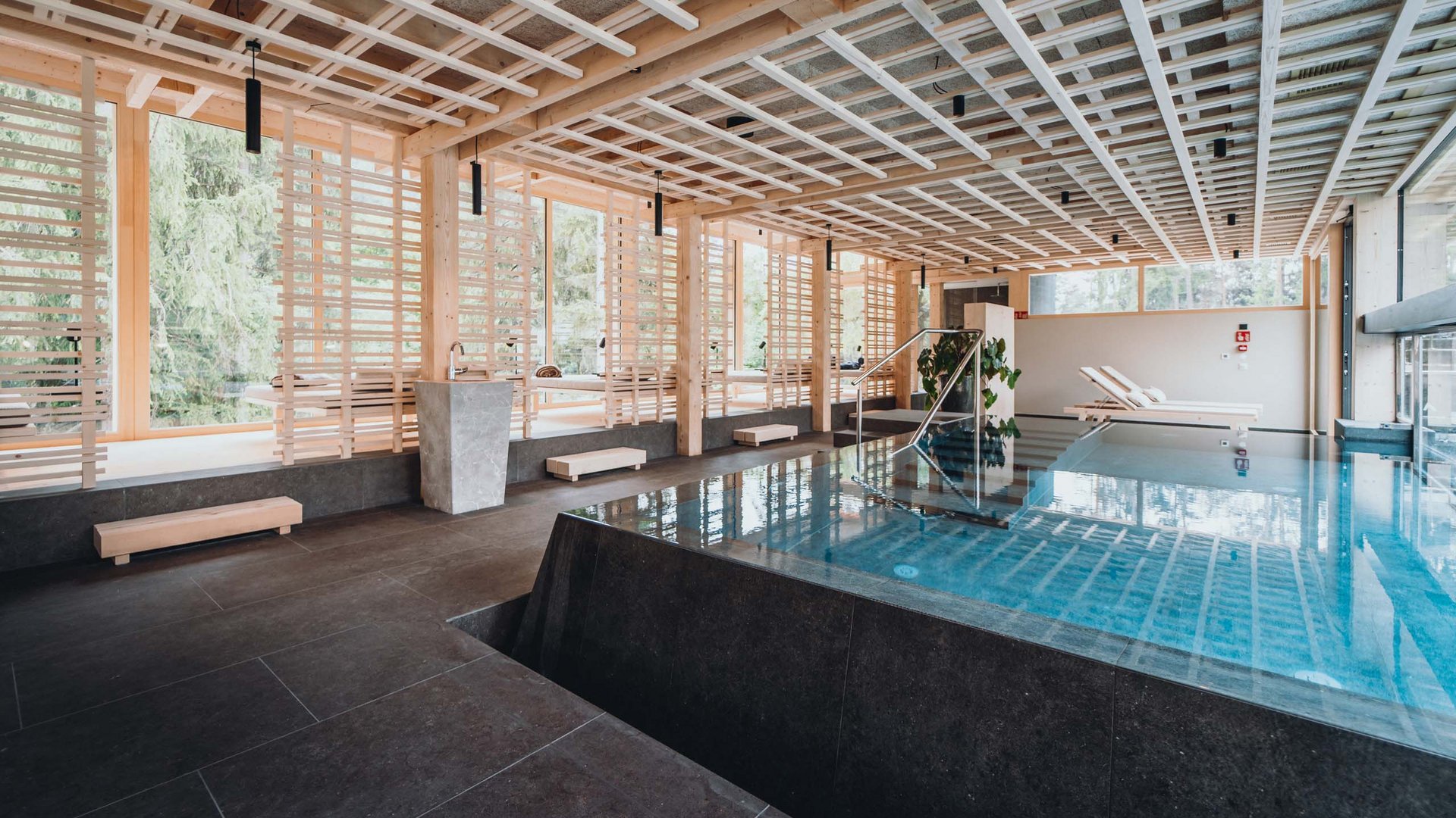A day spa in the Dolomites to soothe your soul Modern indoor pool with wooden ceiling and lounge chairs next to large windows