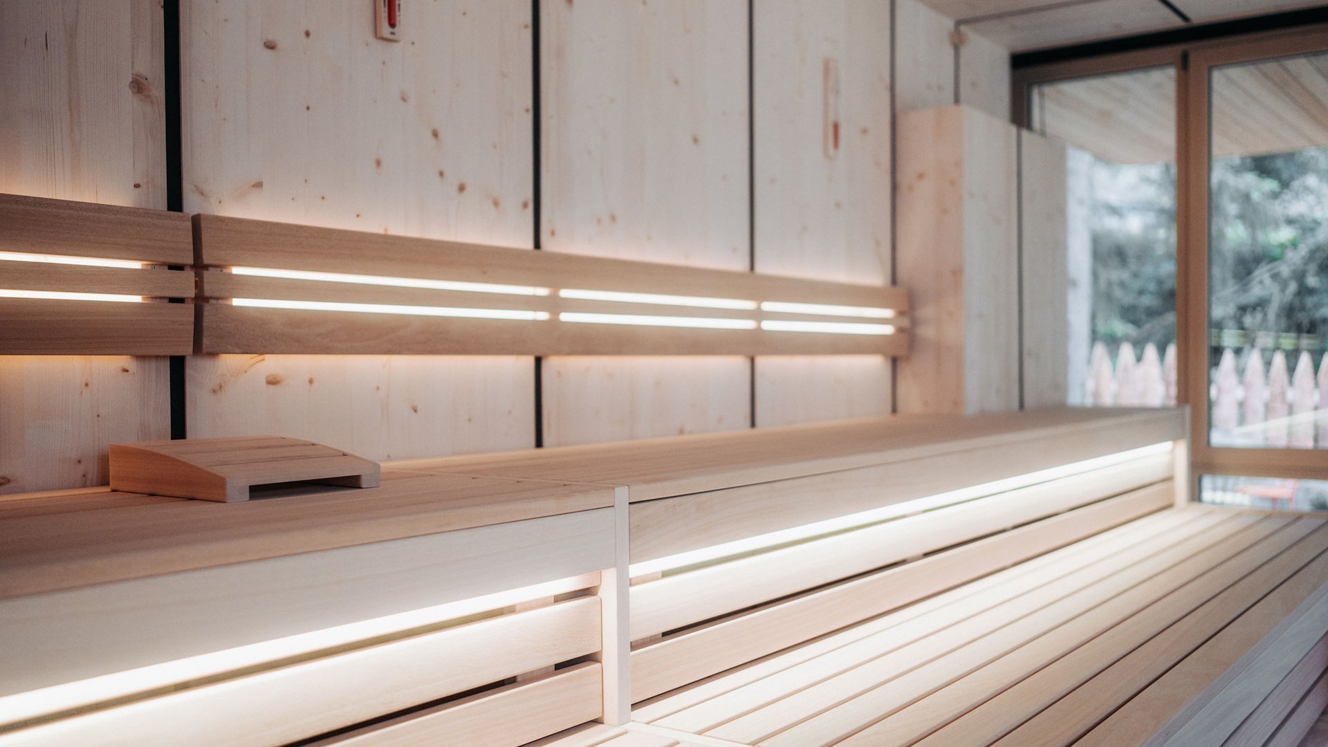 Das Badehaus im Hotel mit Pool in den Dolomiten Innenansicht einer modernen Sauna mit Holz- und indirekter Beleuchtung