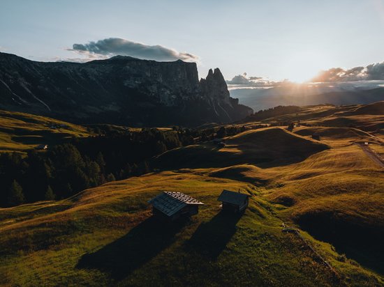Scopri Sciliar: Avventure e Escursioni nel Cuore delle Dolomiti Tramonto su colline verdi con montagne sullo sfondo