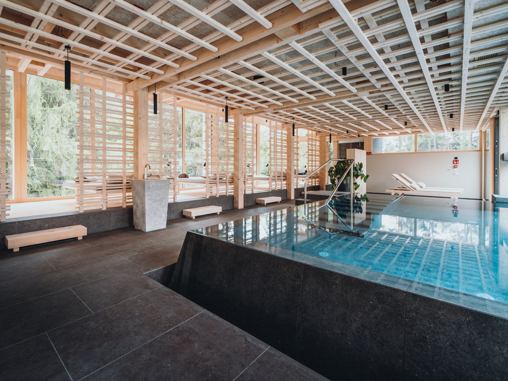 Momente, die bleiben. Im Luxushotel auf der Seiser Alm. Moderner Innenpool in stilvollem Holz- und Steindesign mit Liegestühlen