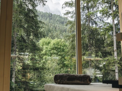 Wellness on Alpe di Siusi/Seiser Alm – Sensoria Dolomites Bench with blanket by large window overlooking forest and mountains